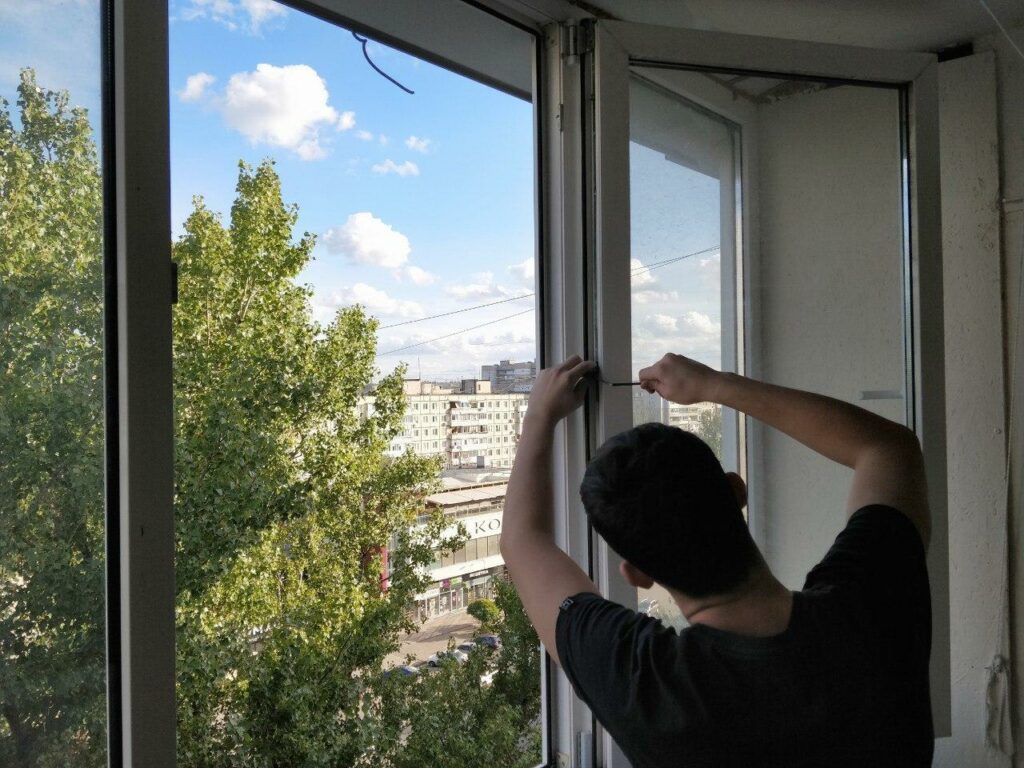 Мастер ремонтирует и настраивает фурнитуру окна перед зимой